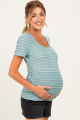 woman wearing a teal striped maternity top and holding her baby bump while posing in black shorts
