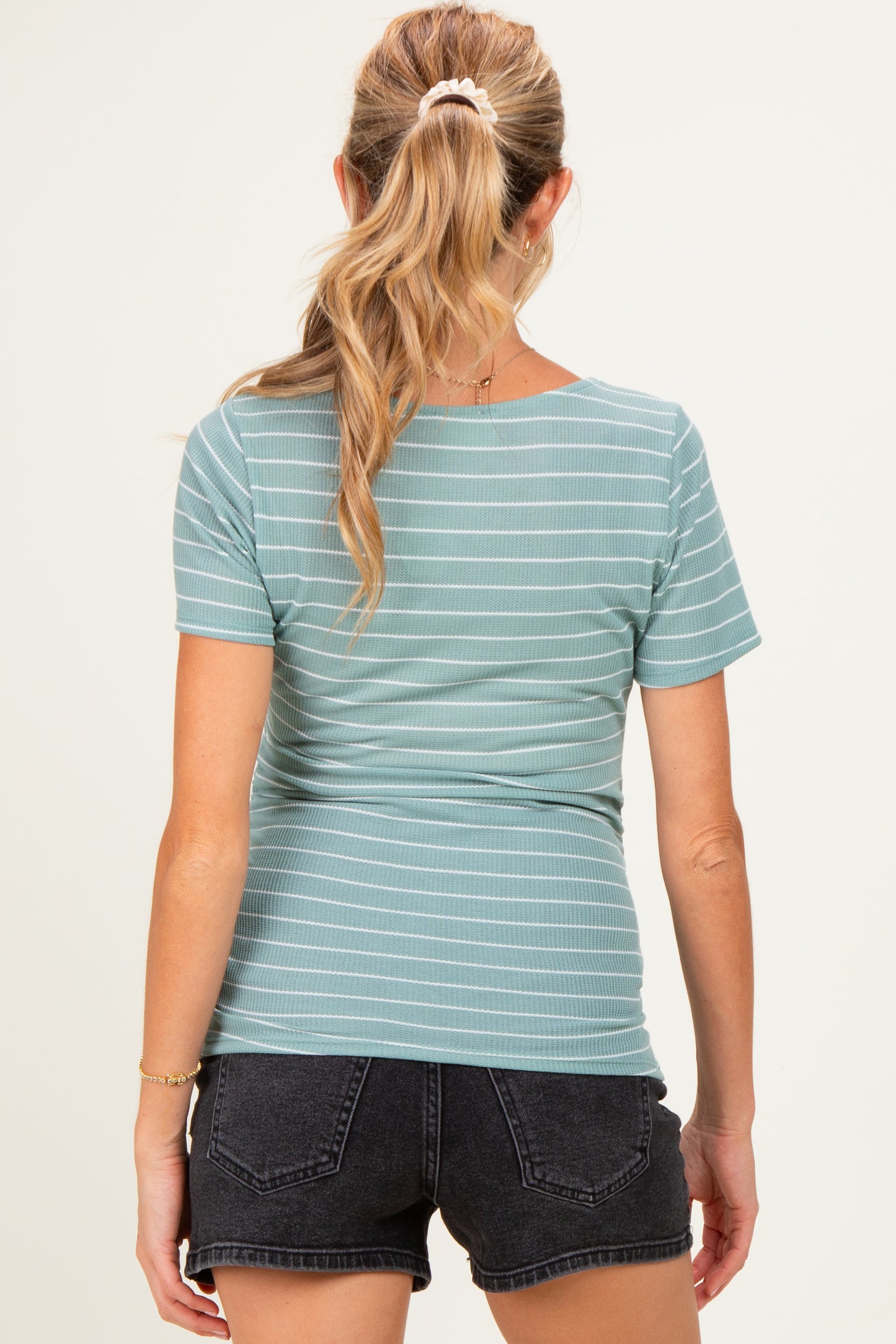 woman wearing a light teal striped maternity top with short sleeves and a fitted style, showing her back