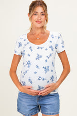 woman wearing a white floral print maternity top and holding her baby bump, paired with denim shorts
