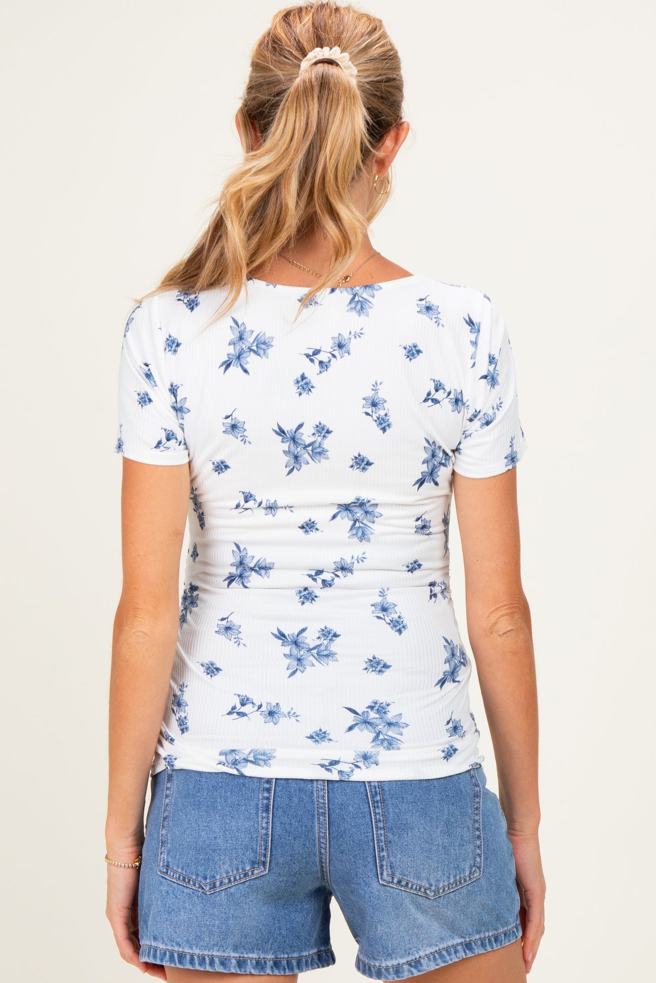 woman wearing a white maternity top with blue floral print and styled hair, paired with denim shorts from the back