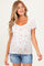woman wearing a white maternity top with a floral print and a visible baby bump, paired with denim shorts