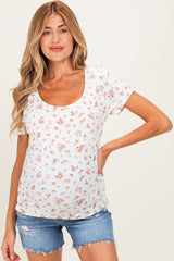 woman wearing a white floral print maternity top and denim shorts, showing her baby bump