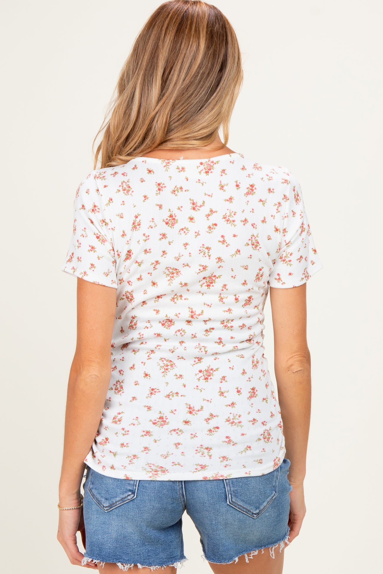 woman wearing a white short sleeve maternity top with a floral print, styled with denim shorts