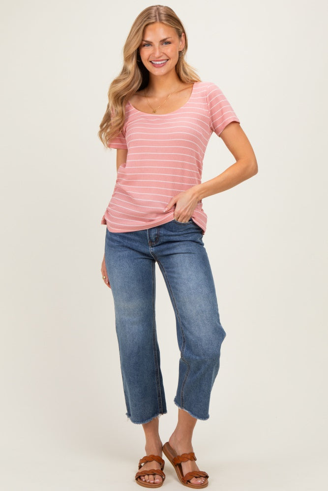 woman wearing a pink striped short sleeve top and blue cropped jeans, standing with one hand on her hip