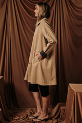 woman wearing a beige long coat with side pockets and a relaxed fit, styled with black shorts and flip flops