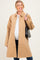 woman wearing a tan button-up maternity coat over a white top, holding a black handbag and showing her baby bump