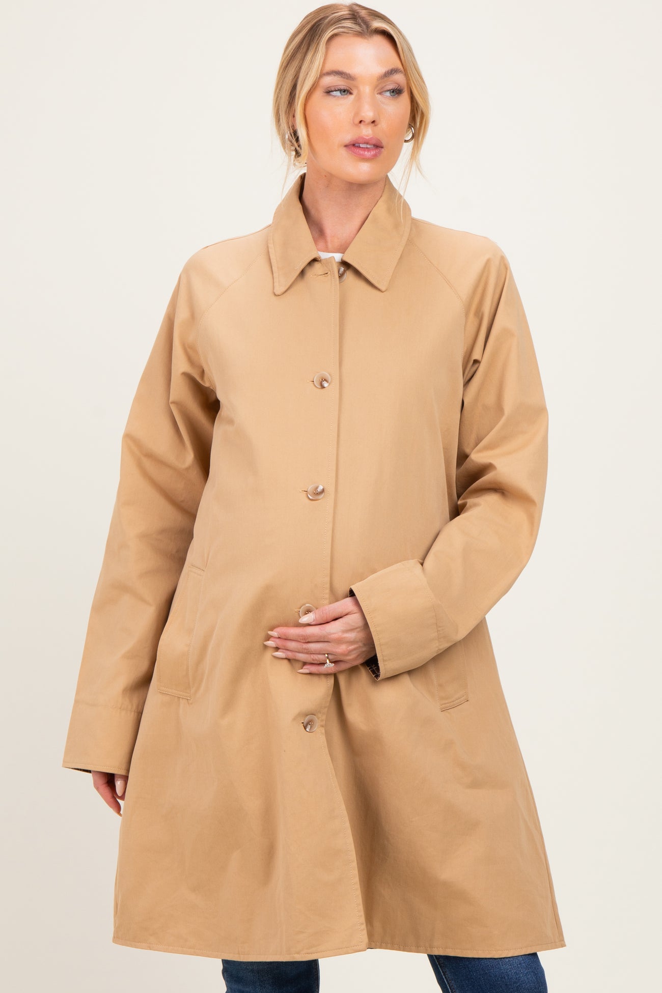 woman wearing a beige maternity coat with button closure and side pockets, holding her baby bump