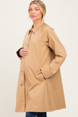 woman wearing a tan maternity coat with a relaxed fit, holding her baby bump on a light background