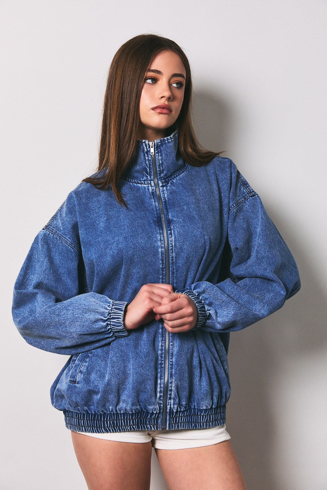 woman wearing a light blue oversized denim jacket with a high collar and elastic hem, styled with white shorts