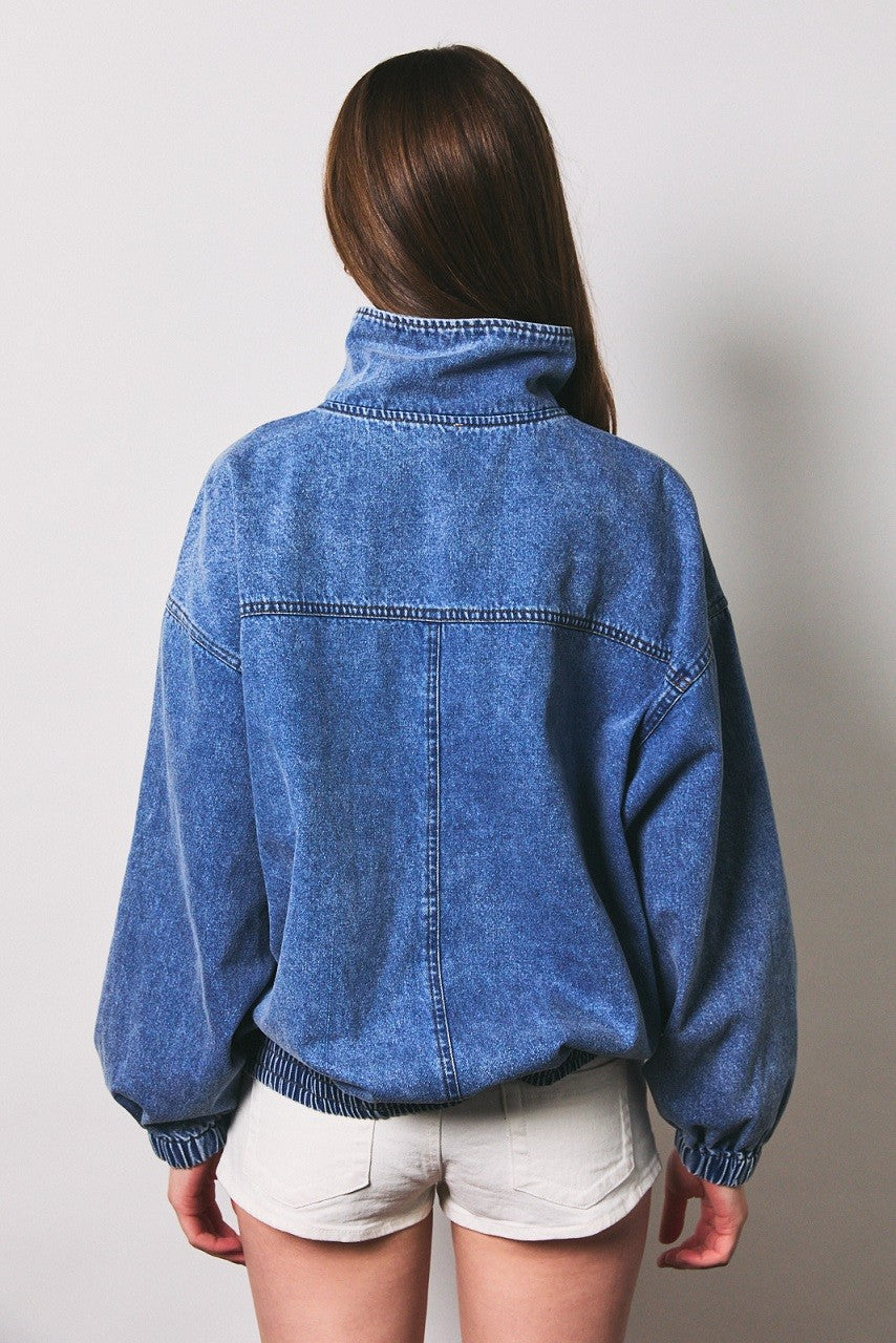woman wearing a loose fit denim jacket with a high collar and elastic waistband, viewed from the back