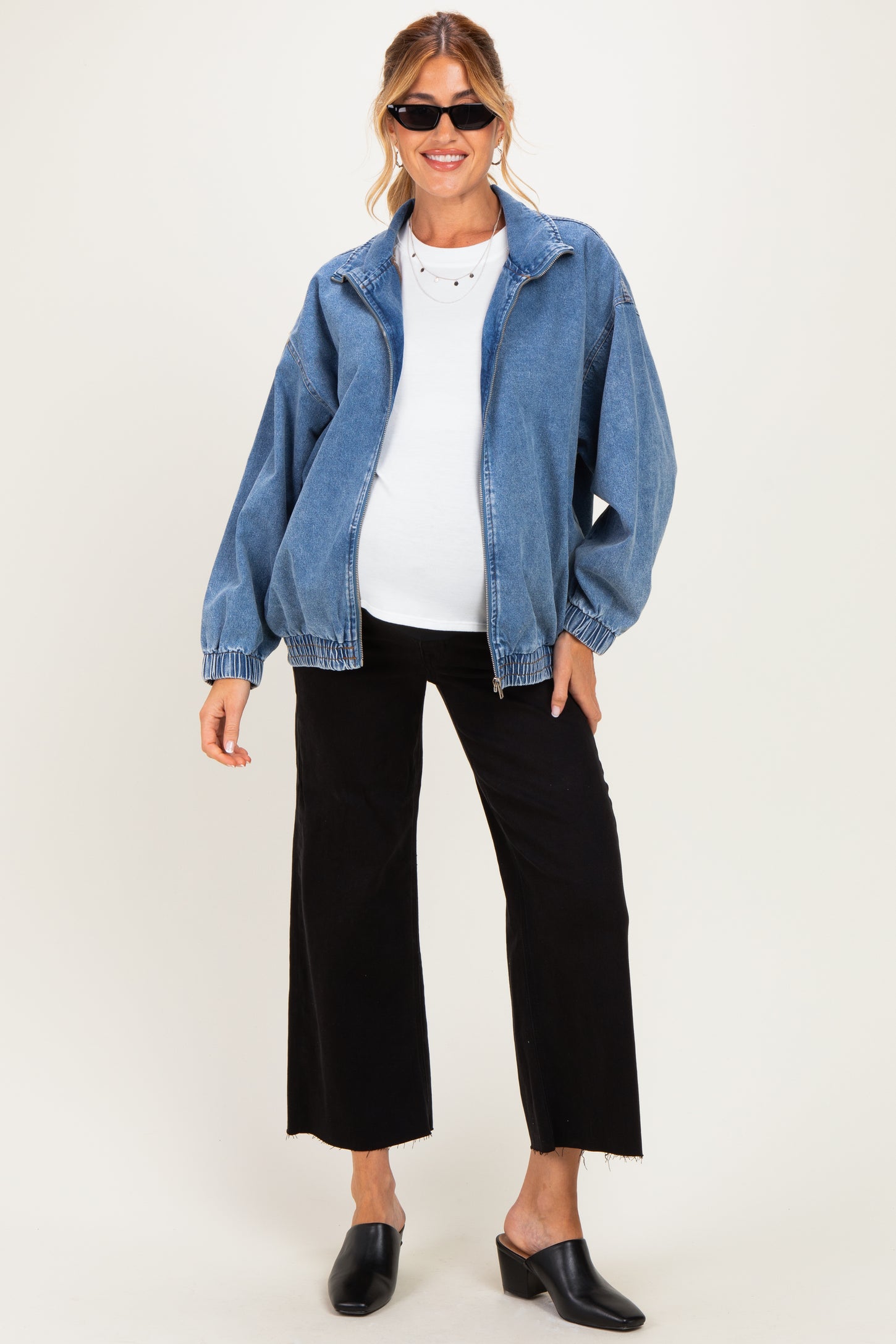 woman wearing a denim maternity jacket over a white top and black wide-leg pants, showing her baby bump