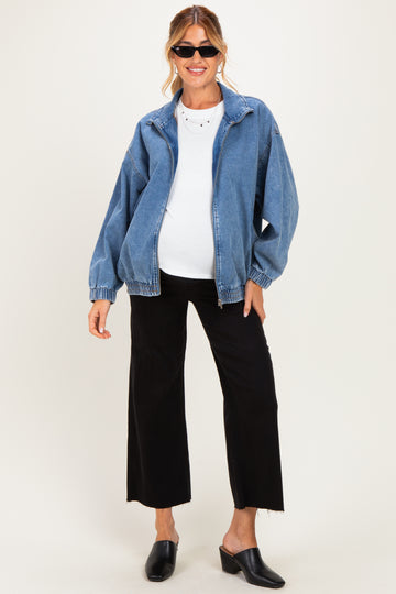 woman wearing a denim maternity jacket over a white top and black wide-leg pants, showing her baby bump
