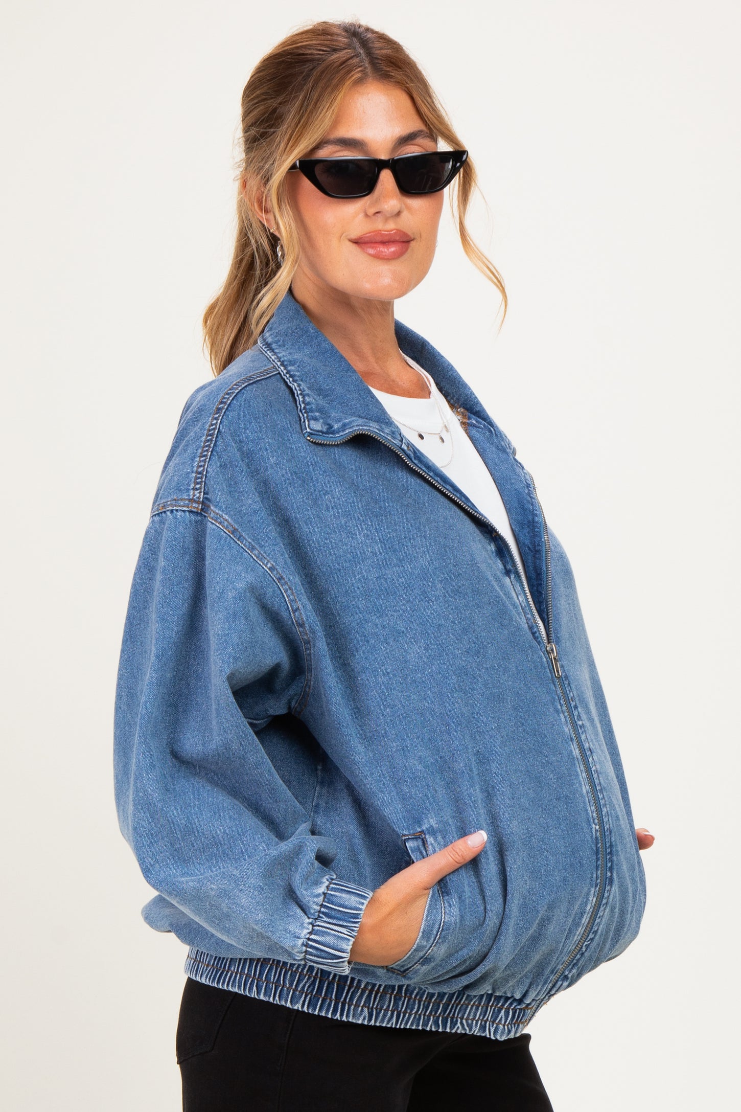 woman wearing a light blue maternity denim jacket with an oversized fit and elastic waistband, styled with black sunglasses