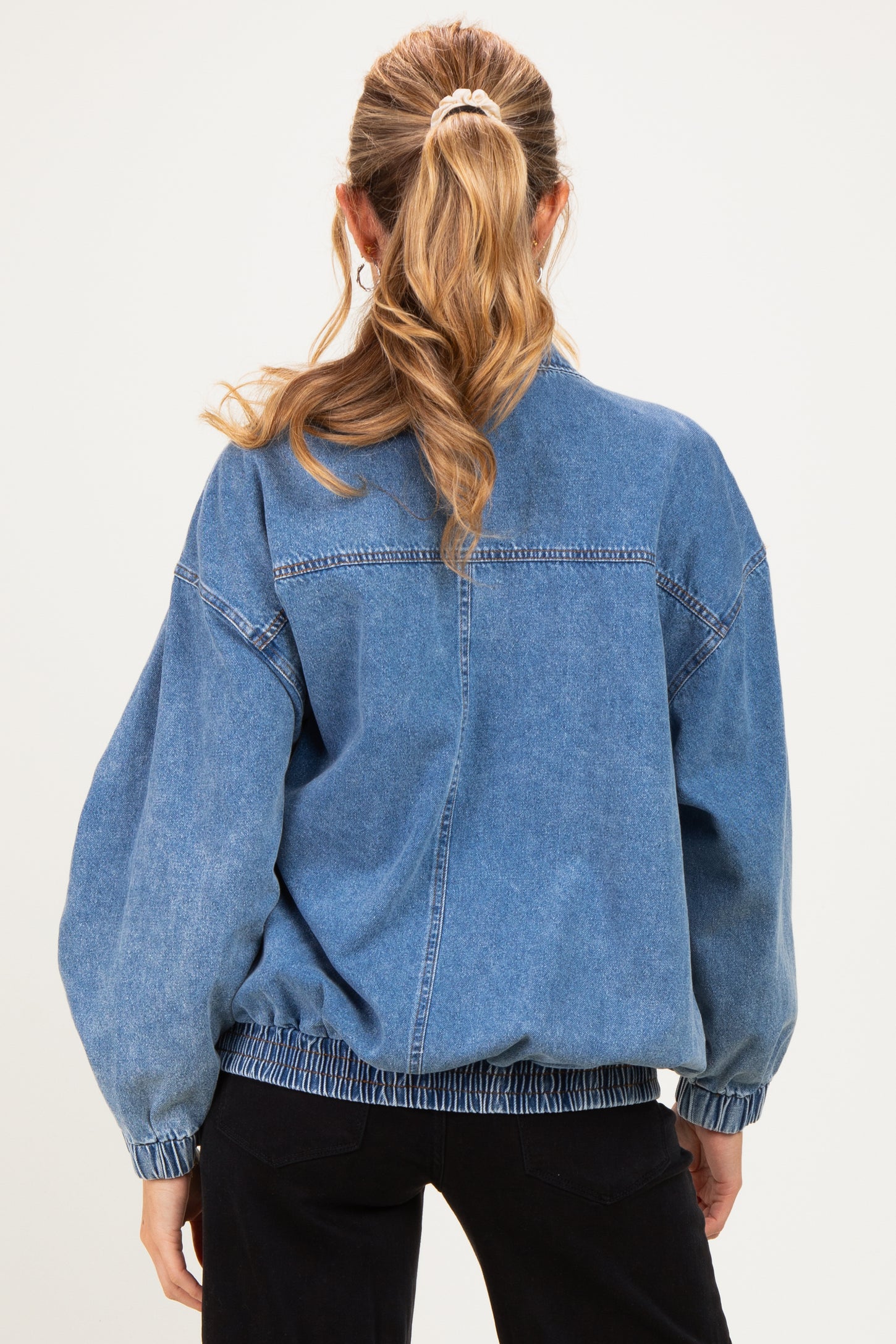 woman wearing a blue oversized denim maternity jacket with elasticized hem and balloon sleeves, showing her back