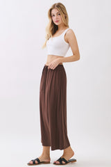 woman wearing a white crop top and brown wide-leg trousers with a drawstring waist and black sandals