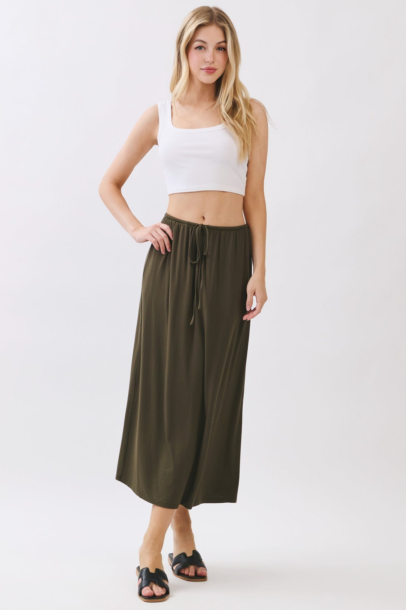 woman wearing an olive green maxi skirt with an elastic waistband and drawstring, paired with a white cropped tank top