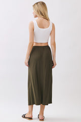 woman wearing a white crop top and an olive green maxi skirt, standing with her back to the camera