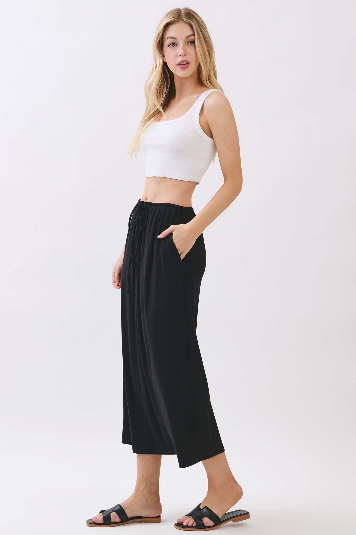 woman wearing a white cropped tank top and black culotte pants with side pockets