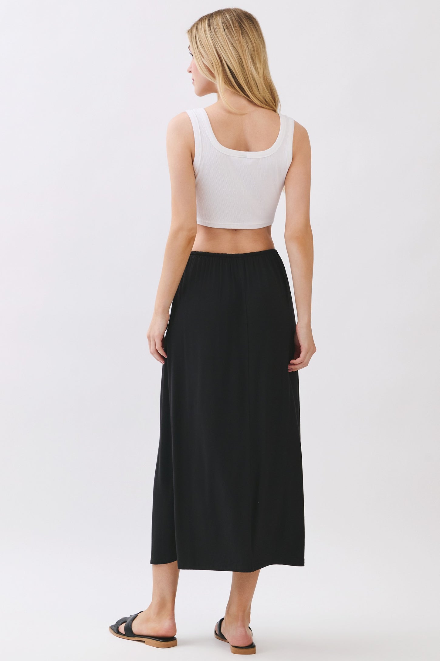 woman wearing a white cropped tank top and a black maxi skirt, viewed from the back