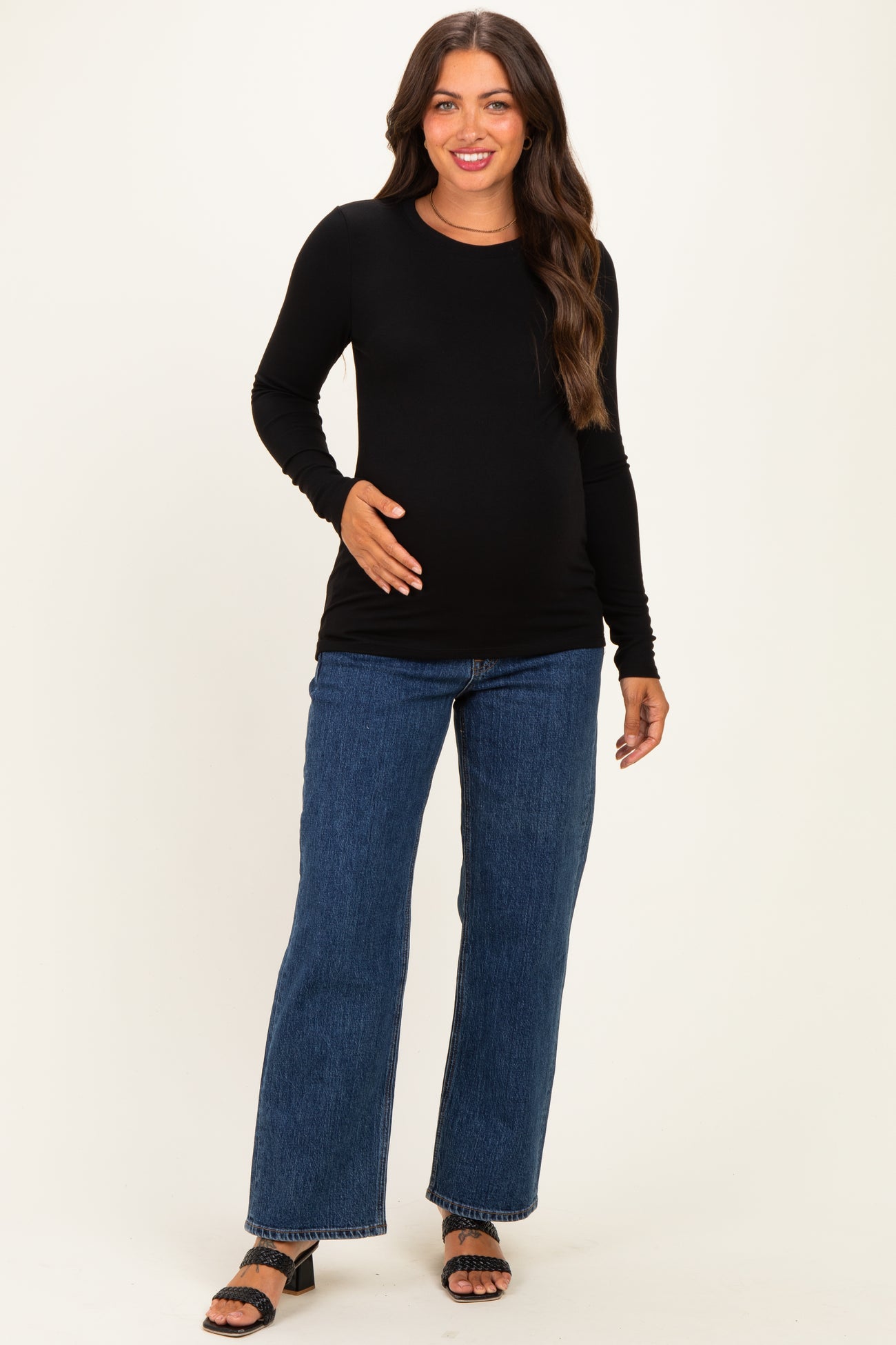 woman wearing a black long sleeve maternity top and blue flared jeans, holding her baby bump