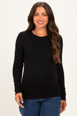 woman wearing a black long sleeve maternity top and smiling, revealing her baby bump