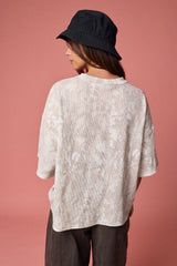woman wearing an oversized beige tie-dye shirt and a black bucket hat, viewed from the back against a pink background