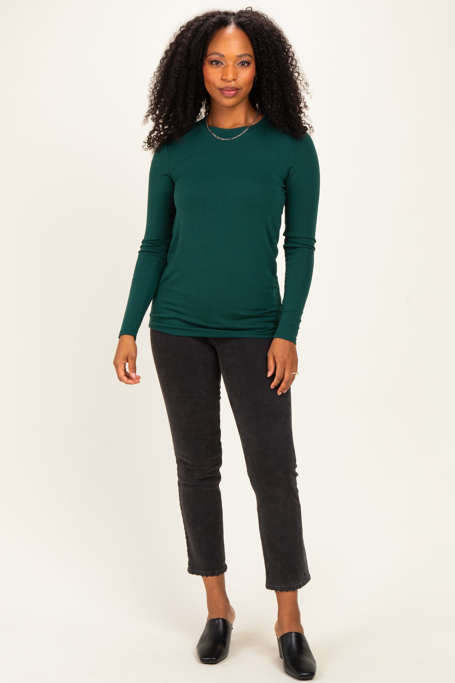 woman wearing a dark green long sleeve fitted top paired with black cropped jeans and slide-on mules