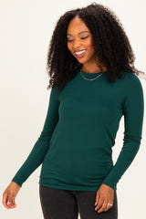 woman wearing a dark green long sleeve fitted top and black jeans, smiling with curly hair down