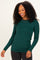 woman wearing a dark green long sleeve fitted top and black jeans, smiling with curly hair down