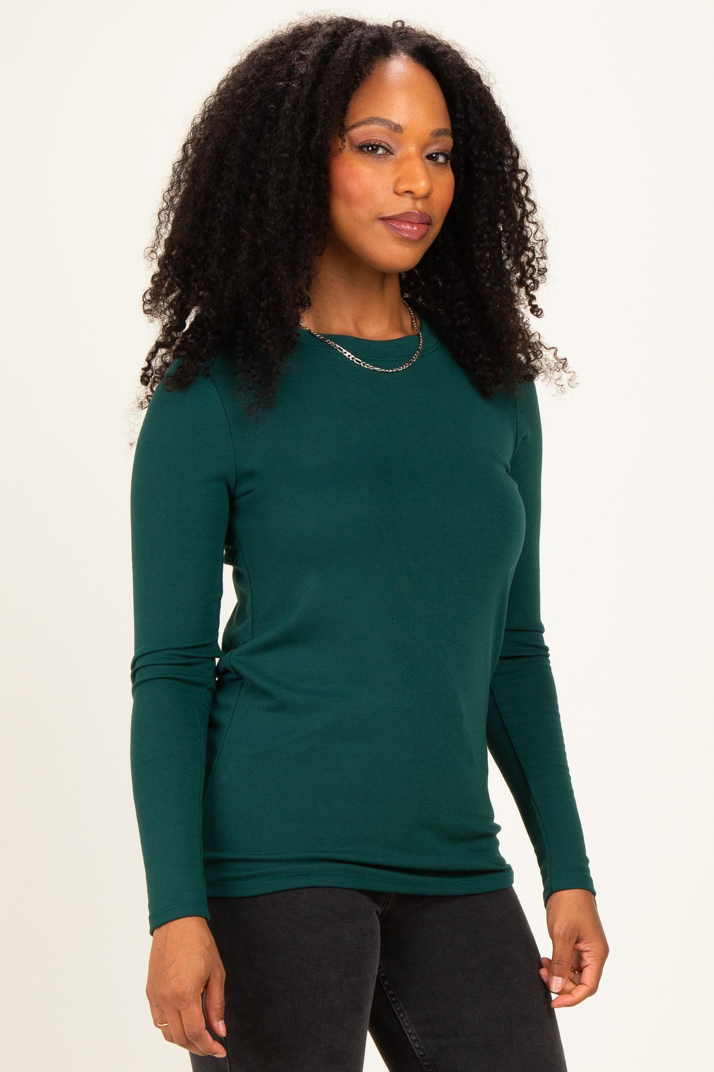 woman wearing a dark green long sleeve fitted top with a round neckline and a slim silhouette
