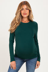 woman wearing a dark green long sleeve maternity top and showing her baby bump while smiling
