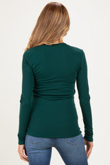 woman wearing a dark green long sleeve maternity top with a fitted silhouette and ruching at the back