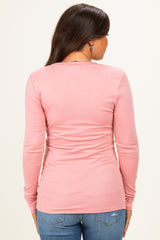 woman wearing a light pink long sleeve maternity top, shown from the back, paired with blue jeans