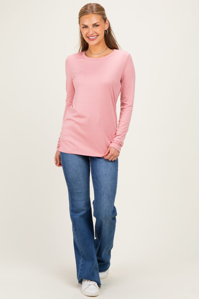 woman wearing a light pink long sleeve top and flared blue jeans, smiling in a neutral background