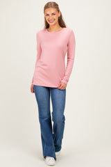 woman wearing a light pink long sleeve top and flared blue jeans, smiling in a neutral background