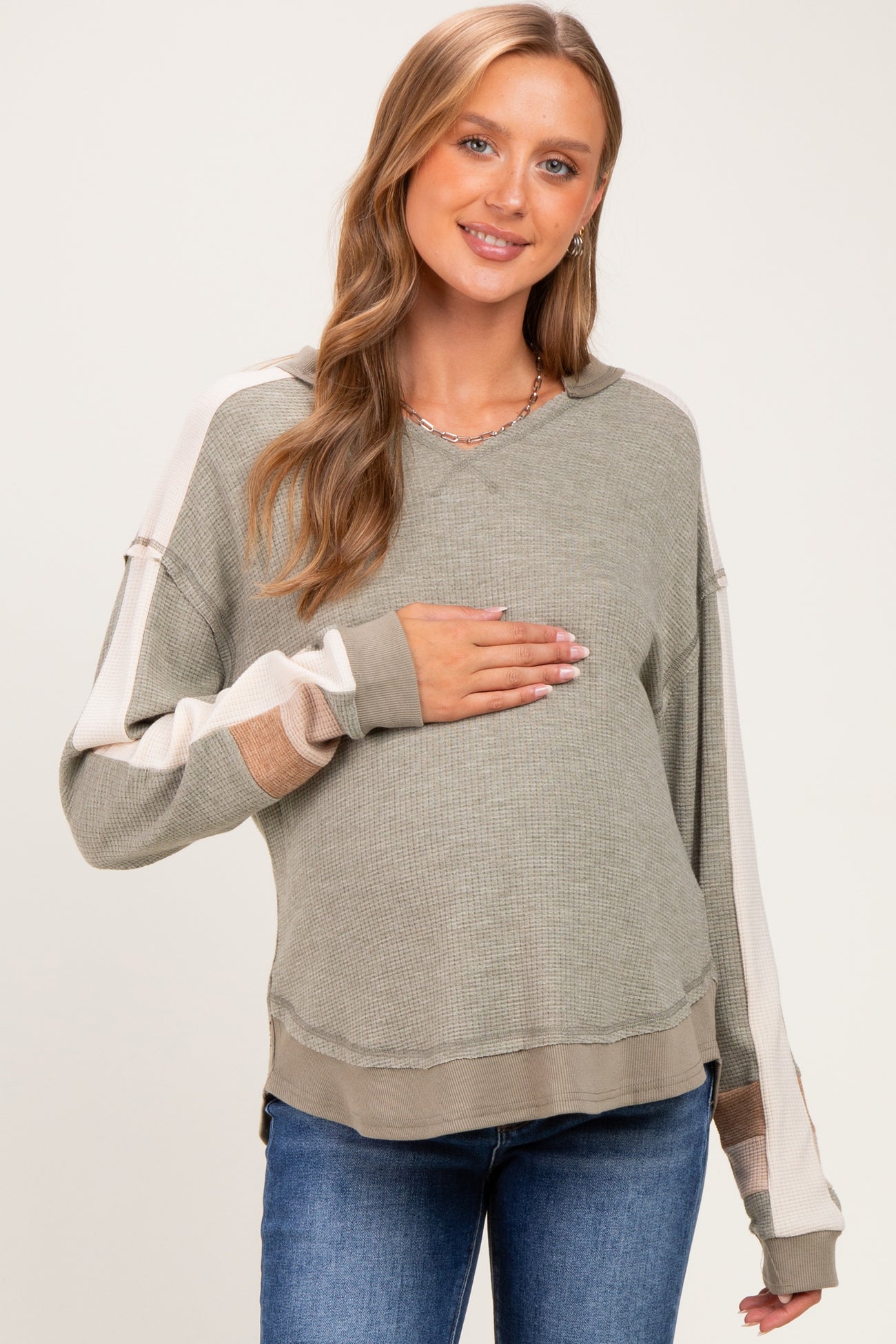 woman wearing a green and beige long sleeve maternity sweater and holding her baby bump