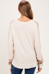 woman wearing a cream-colored long sleeve maternity top with color-blocked sleeves, showing the back view