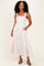woman wearing a white floral maxi dress with purple straps and pockets, styled with black strappy heels