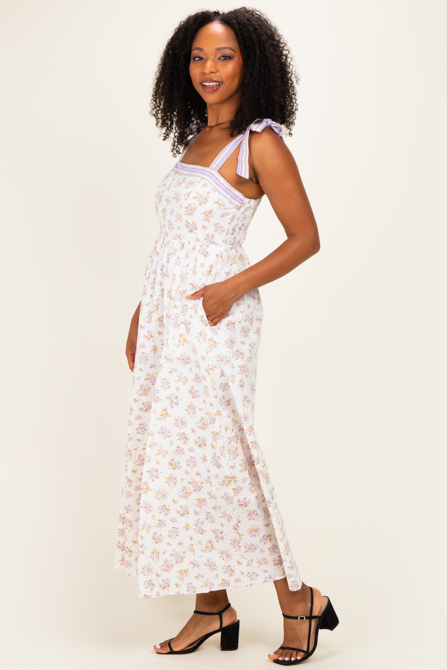 woman wearing a white floral maxi dress with lavender straps and side pockets, standing against a light background