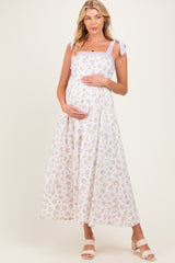 woman wearing a white floral maternity maxi dress with lavender ribbon straps and holding her baby bump