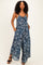 woman wearing a navy blue floral print jumpsuit with wide legs and pockets, standing on a light background