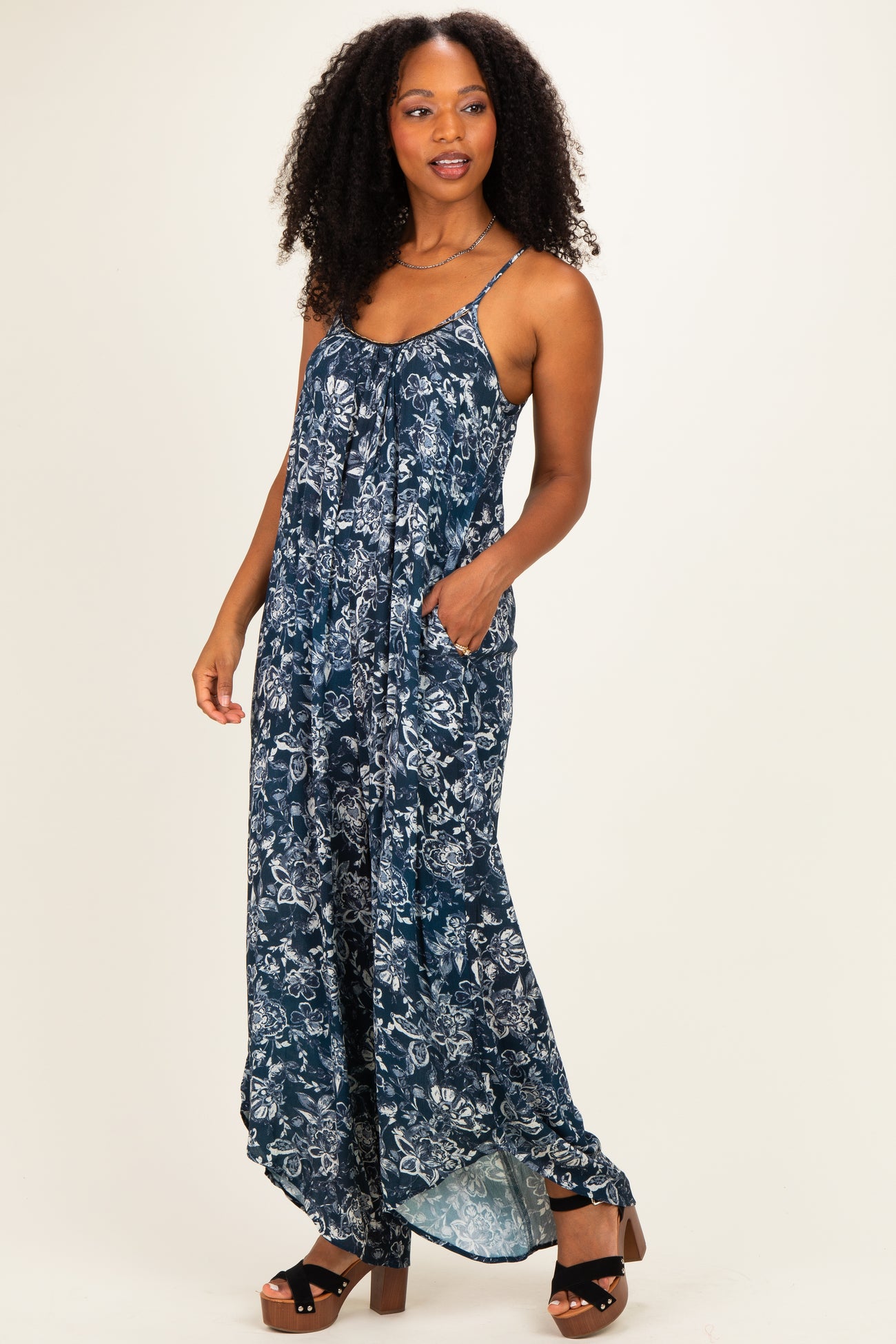 woman wearing a navy blue floral maxi dress with spaghetti straps and pockets, standing confidently