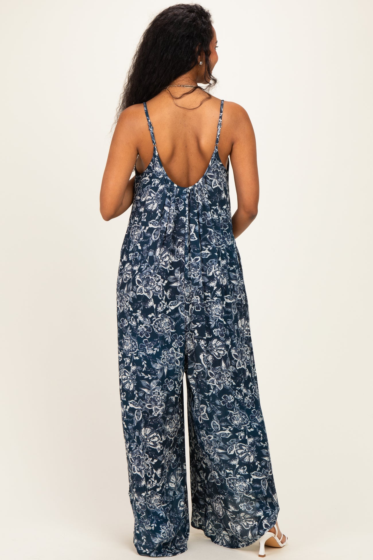 woman wearing a navy floral patterned maternity jumpsuit seen from the back with adjustable spaghetti straps