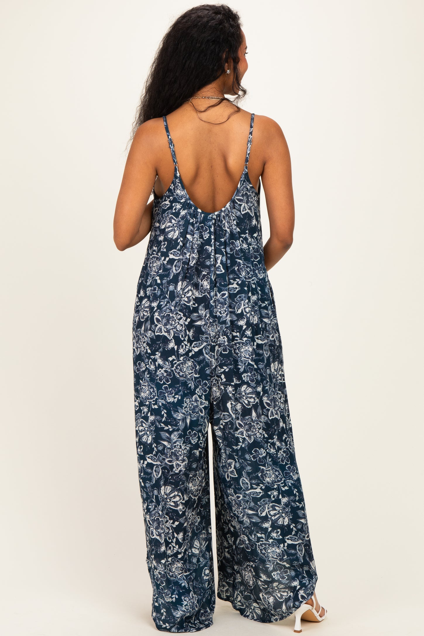 woman wearing a navy floral patterned maternity jumpsuit seen from the back with adjustable spaghetti straps