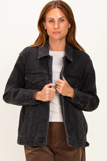 woman wearing a black denim jacket over a white top, holding the jacket closed with both hands