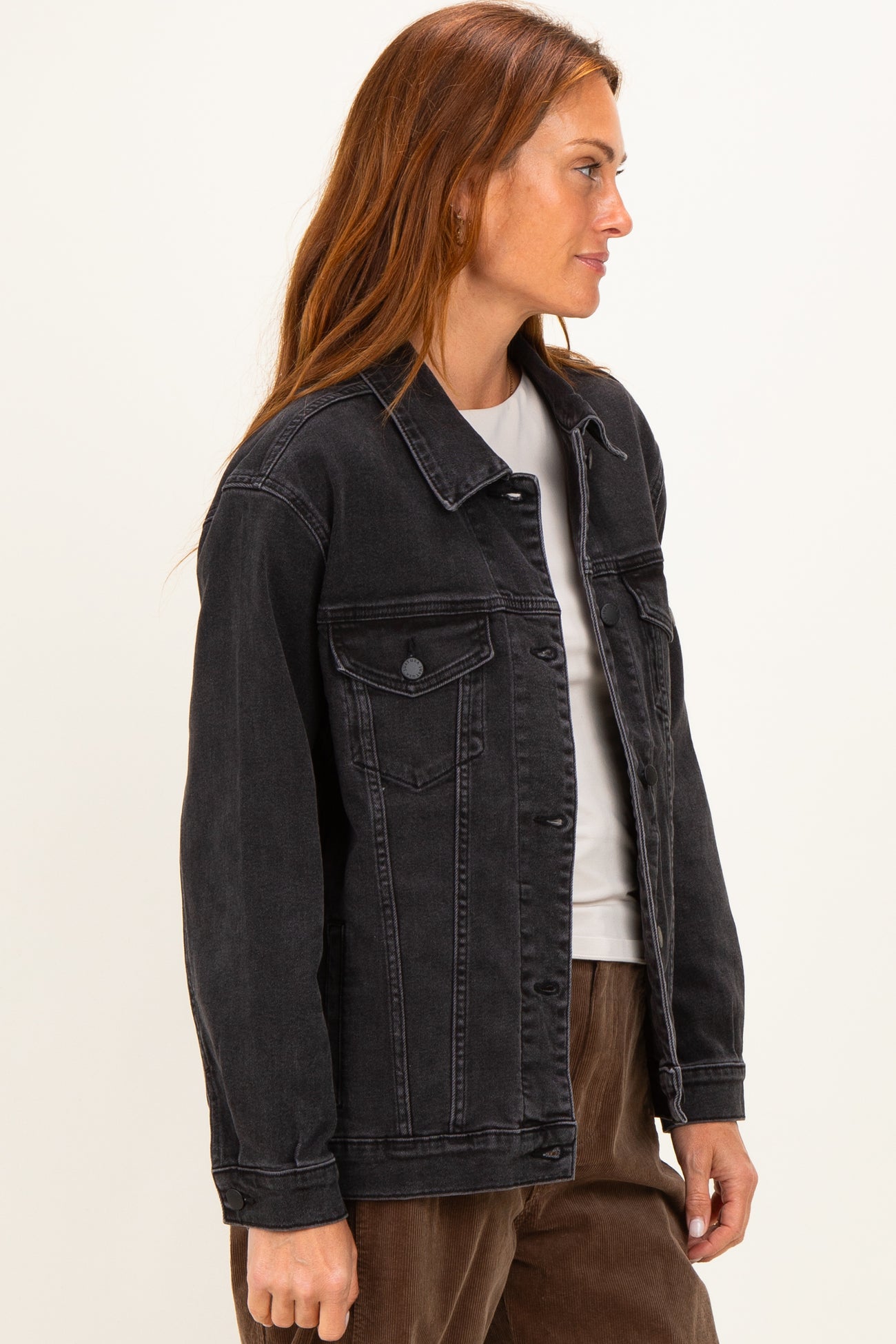 woman wearing a black denim jacket with side pockets and button closure, styled with a white top underneath