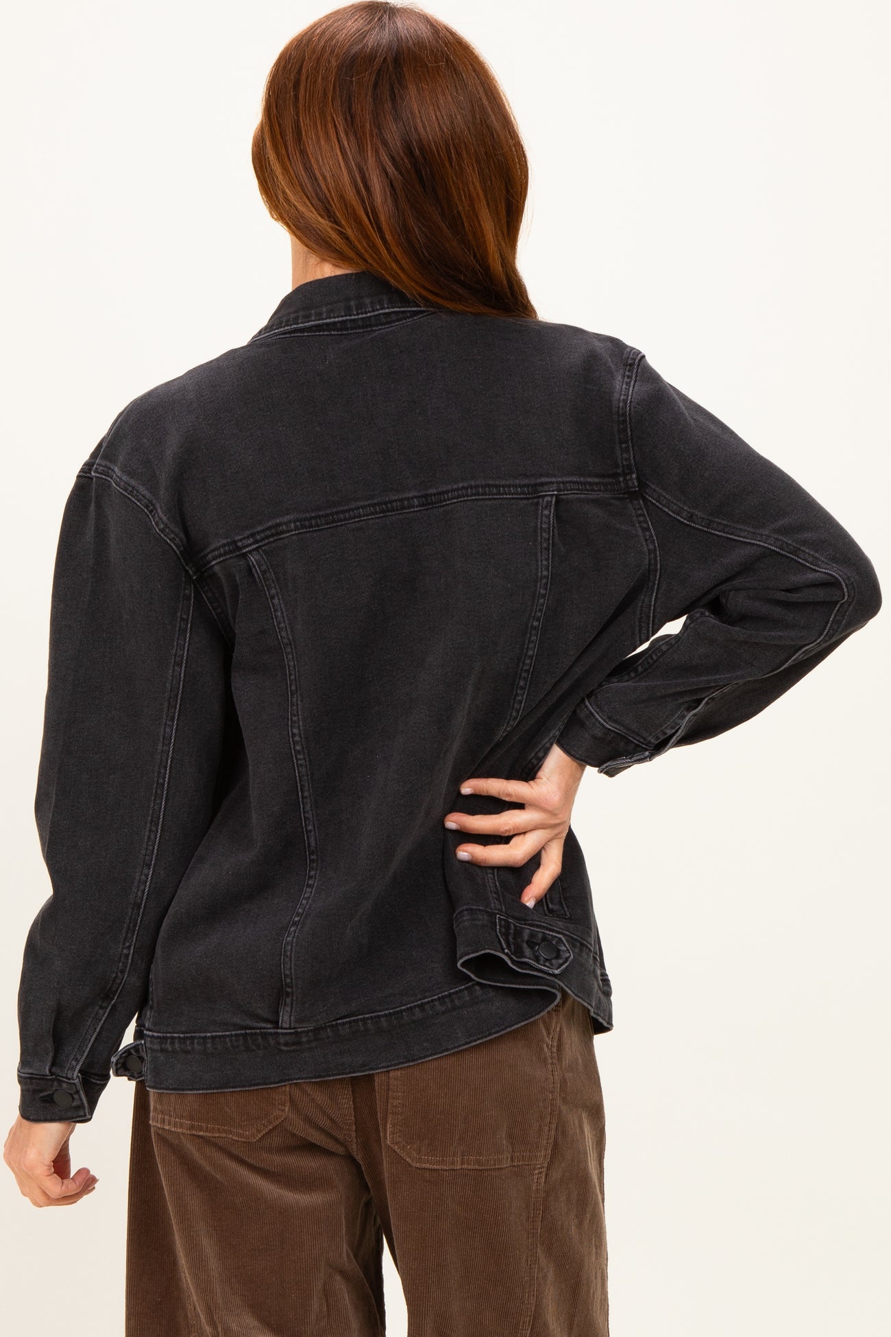 woman wearing a black oversized denim jacket, showing the back view with a relaxed fit and long sleeves