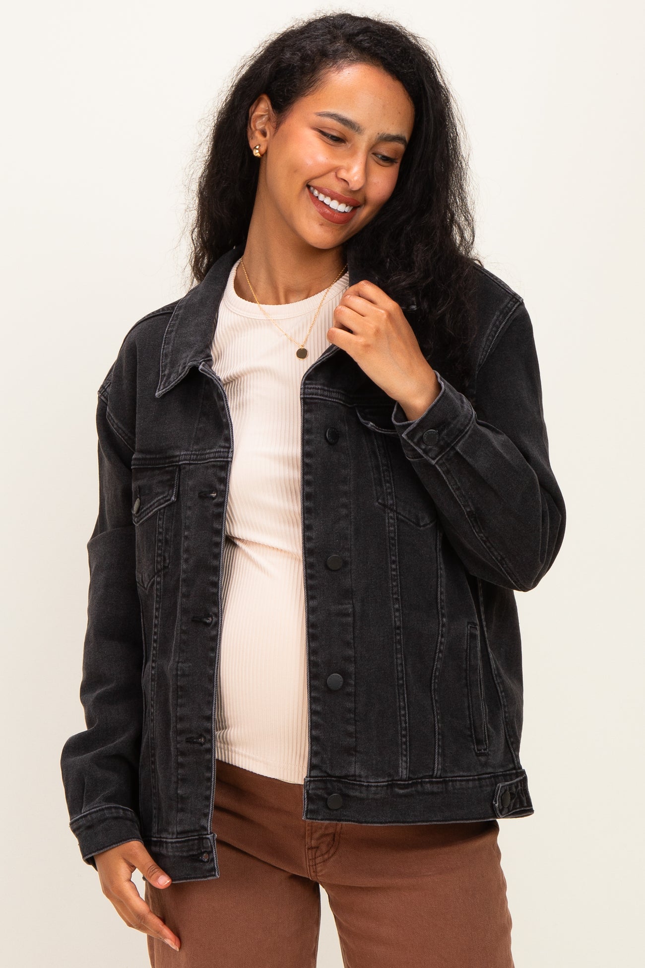 woman wearing a black maternity denim jacket over a light pink top and showing her baby bump