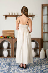 woman wearing a cream-colored maxi dress with a smocked bodice and thin straps, viewed from the back