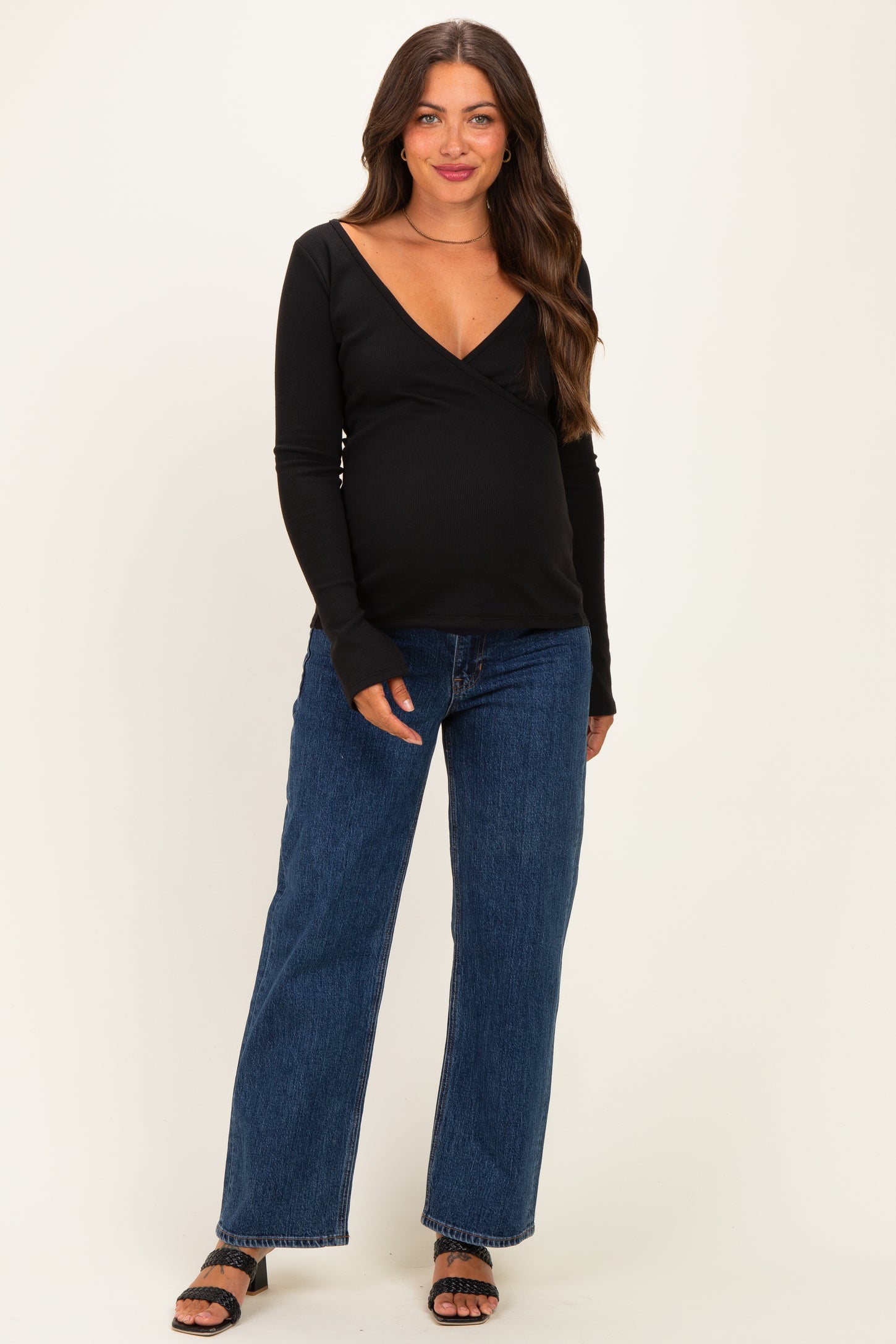 woman wearing a black long sleeve maternity top and blue wide-leg jeans, with a visible baby bump